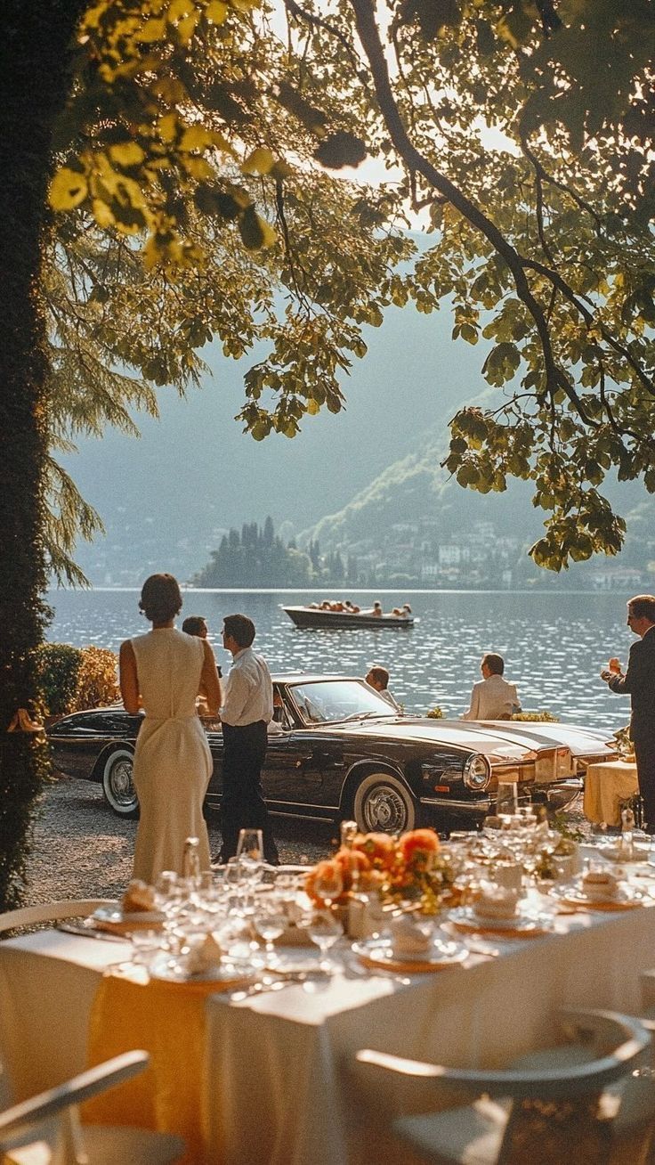 People gathered by a lake with a vintage car and a set table at golden hour