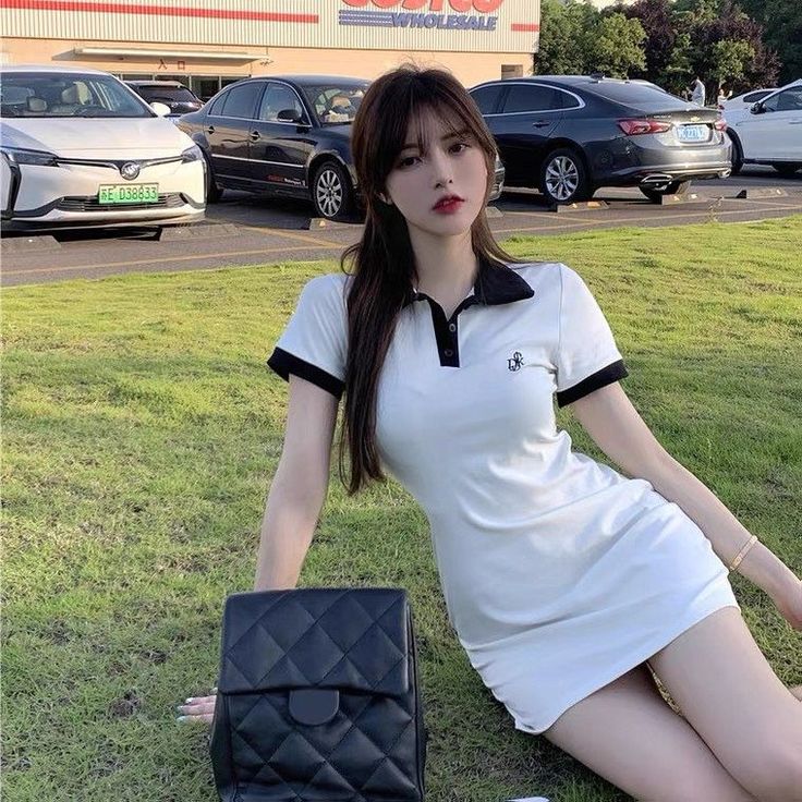 Woman in a white polo dress sitting on grass in a parking lot