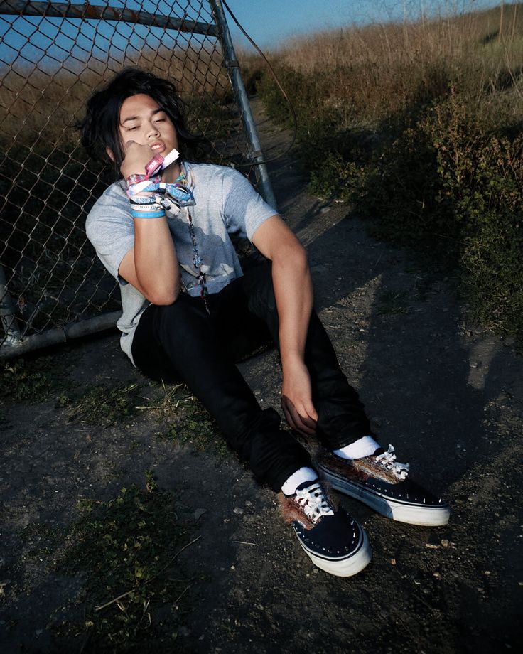 Person with long hair sitting on the ground next to a chain link fence