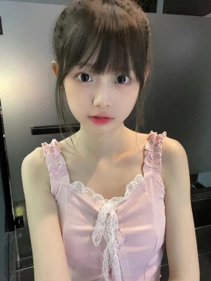 Young woman with dark hair and bangs wearing a pink top with lace trim