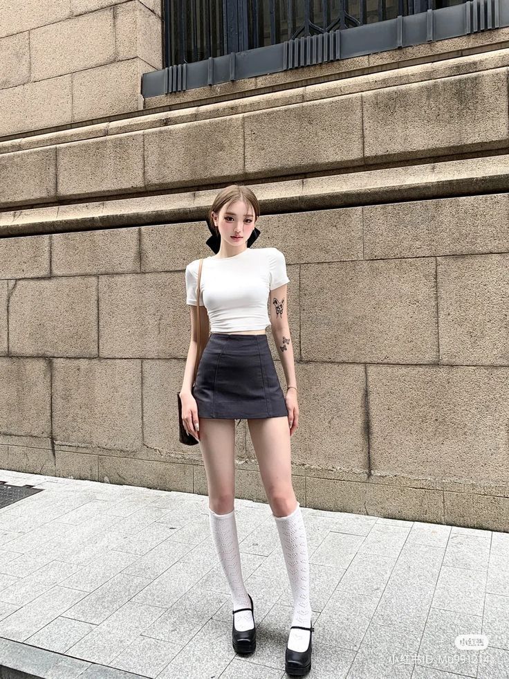 Woman in a crop top and mini skirt with knee-high socks standing outdoors