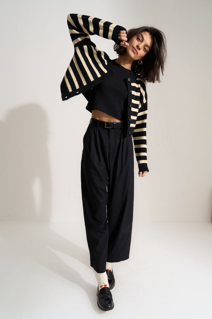 Woman in a striped cardigan, black crop top, and wide leg pants posing in a studio