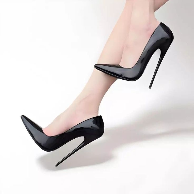Pair of black patent leather high heels on bare legs against a white background