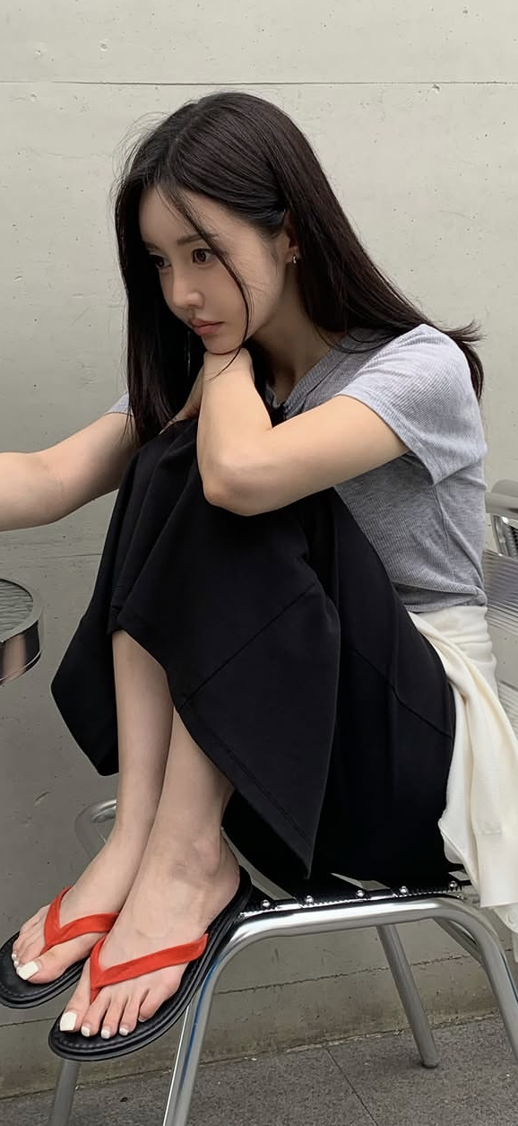 Woman with long black hair wearing a grey t-shirt and black skirt, sitting outdoors