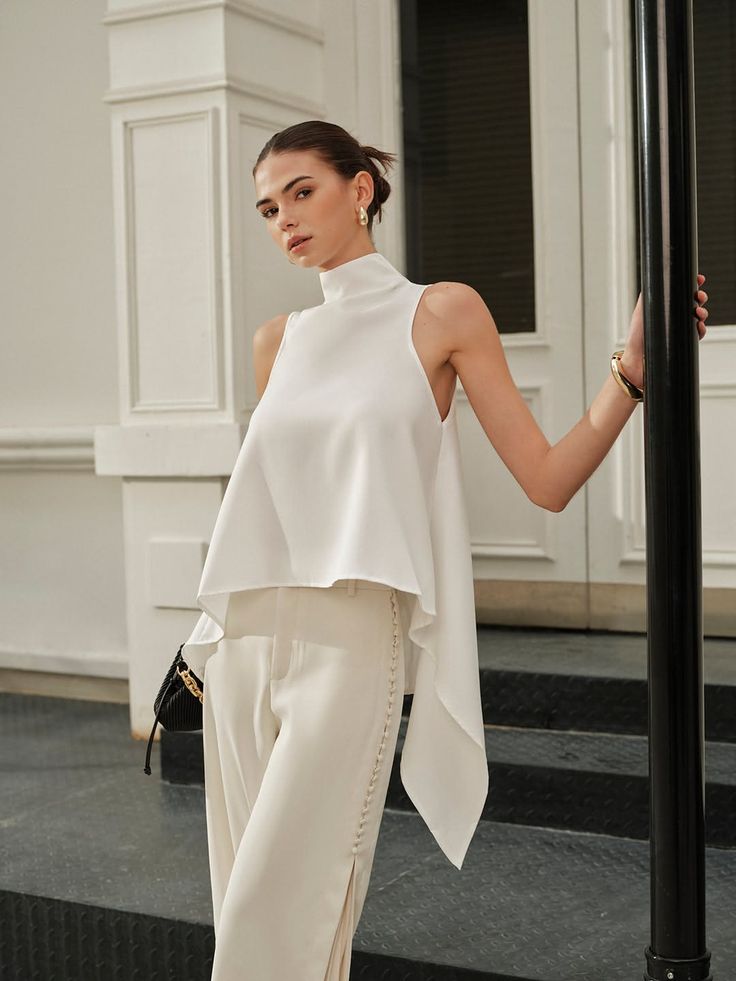 Woman in a white high-neck top and wide-leg pants posing outdoors