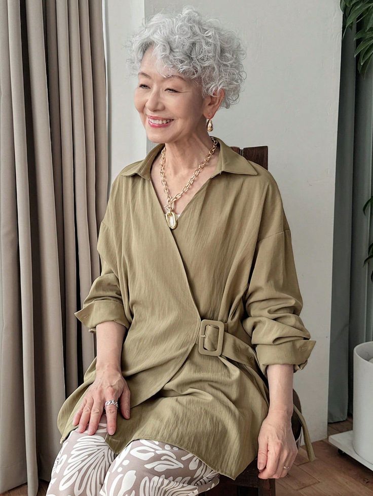Woman with curly silver hair wearing a khaki dress and jewelry, smiling indoors
