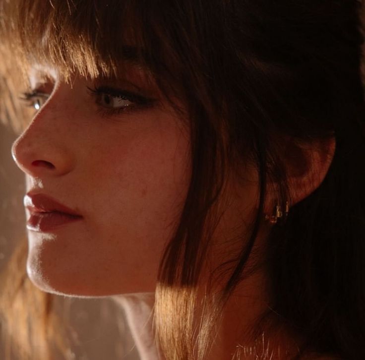 Woman with brown hair and bangs in a close-up profile view with warm lighting
