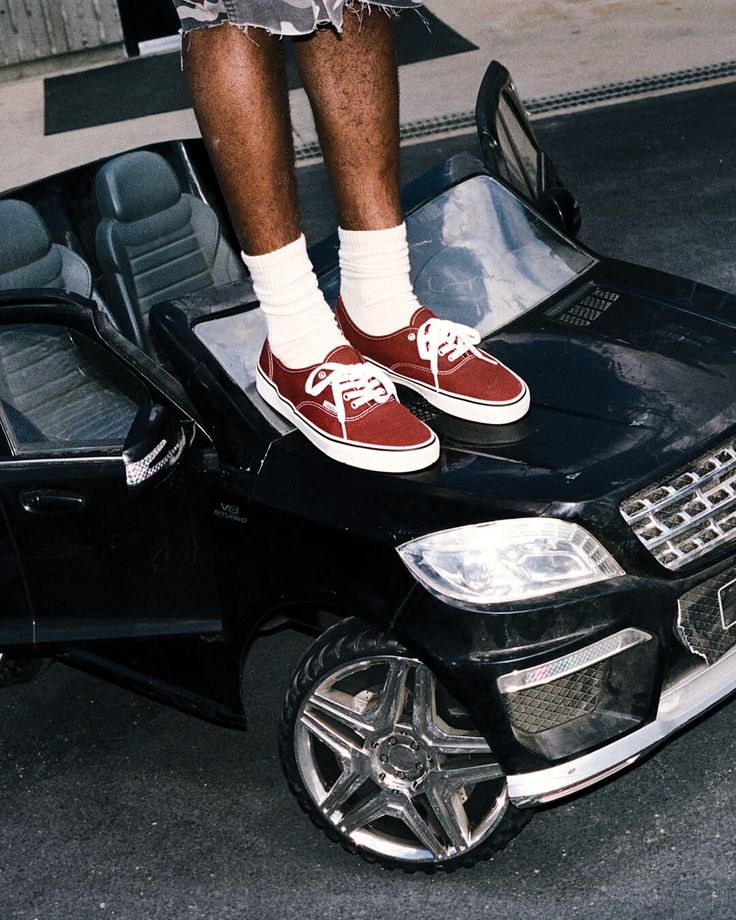 Person standing on a black toy car wearing red sneakers and white socks