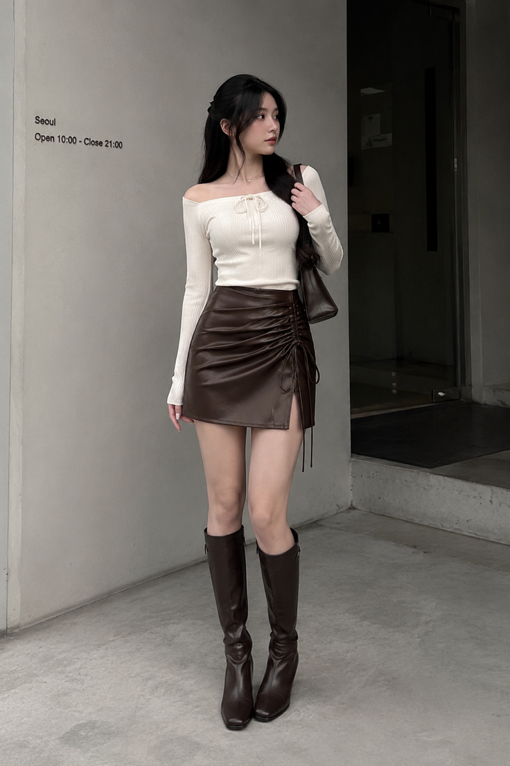 Woman in an off-shoulder top and brown mini skirt with knee-high boots outdoors