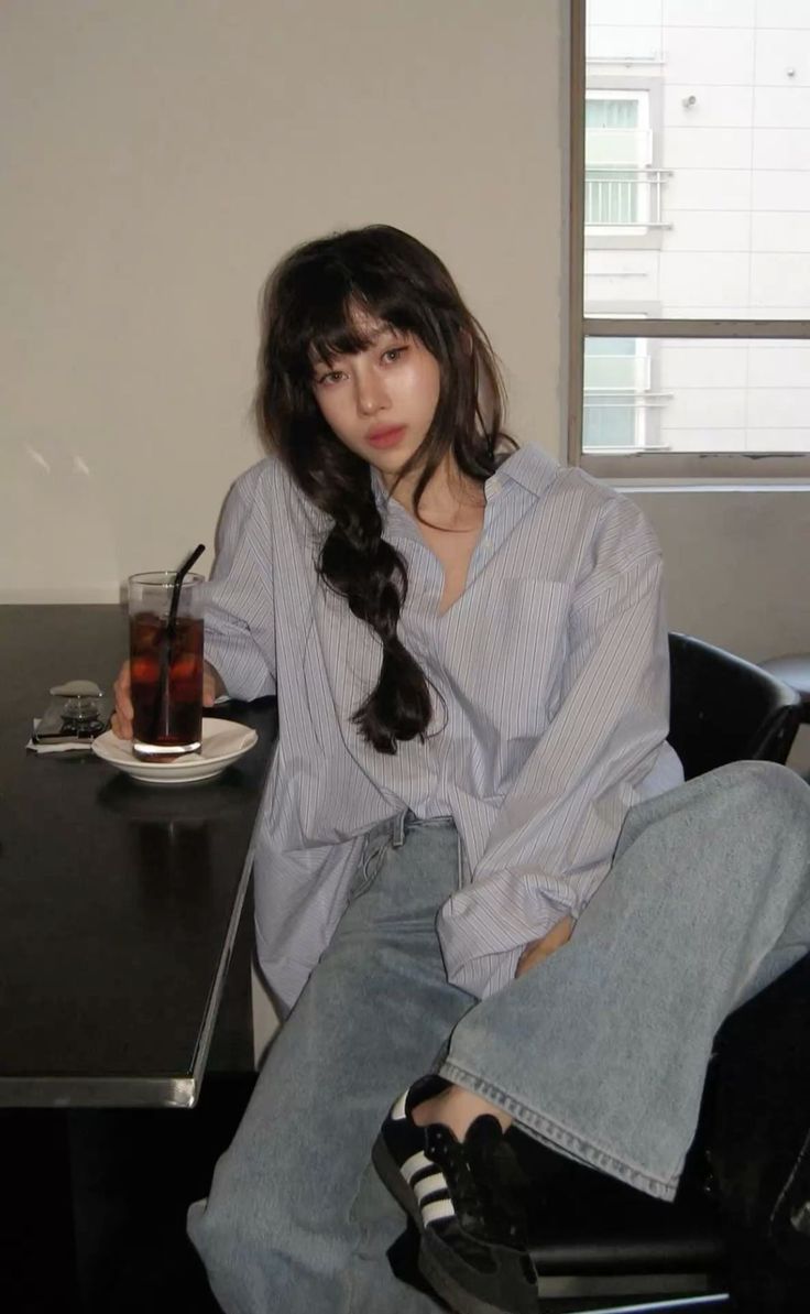 Woman with long dark hair in a striped shirt and jeans holding a drink