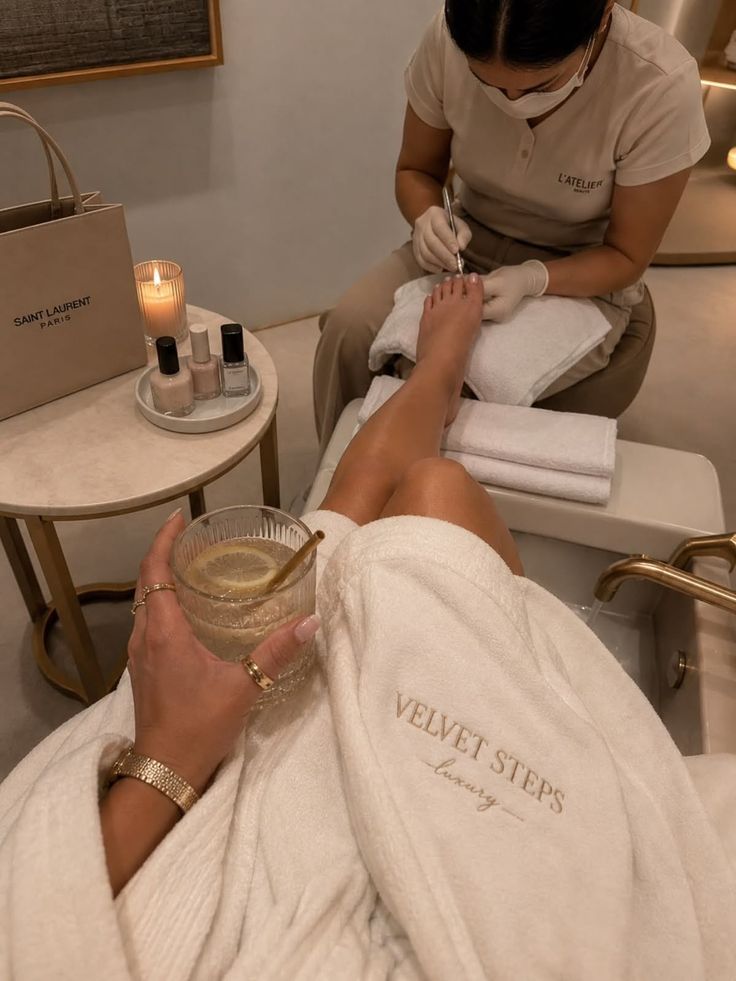 Person getting a pedicure while wearing a white bathrobe and holding a lemon drink