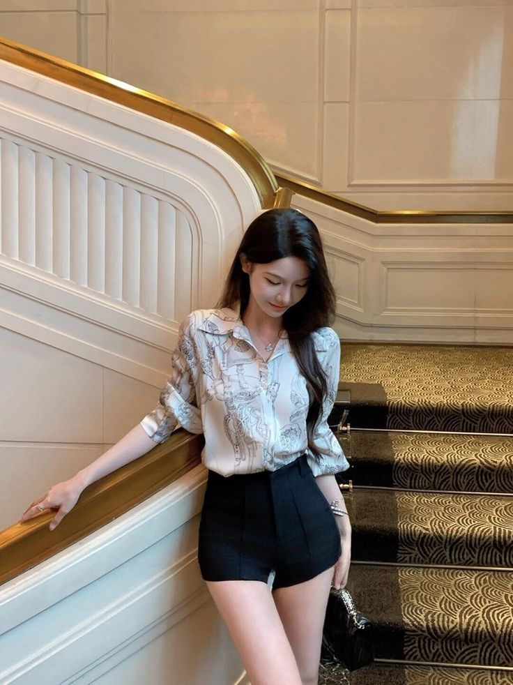 Woman in a patterned shirt and black shorts standing on an elegant staircase
