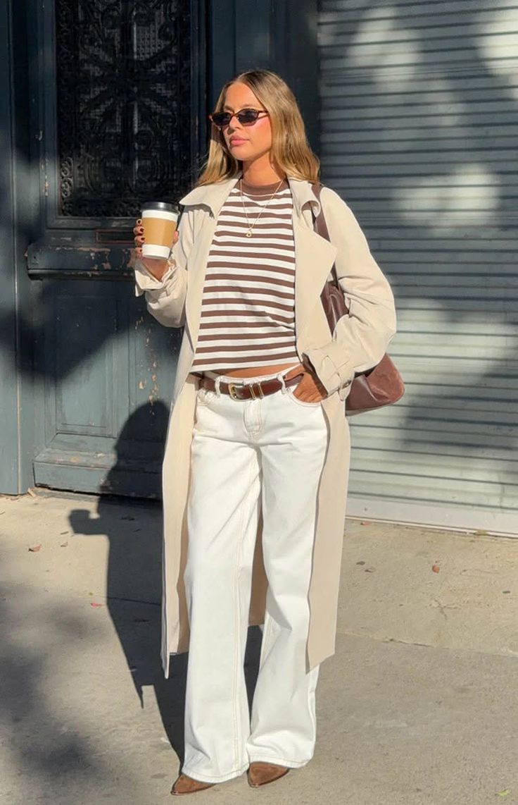 Woman in a trench coat and striped shirt holding a coffee cup outdoors