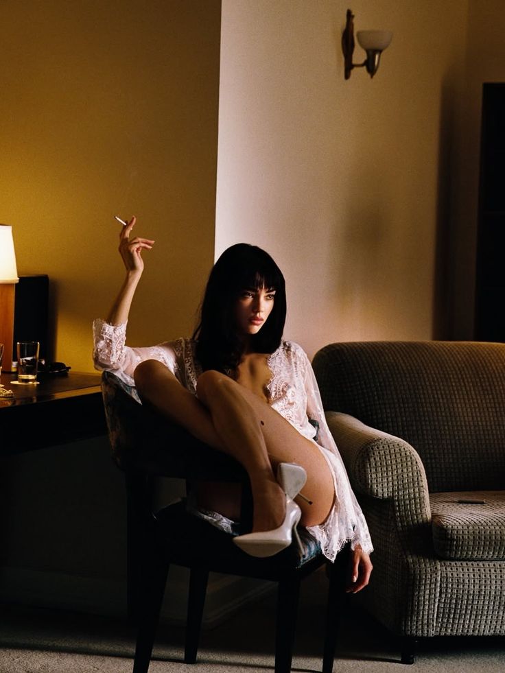 Woman in white lace lingerie and high heels, holding a cigarette indoors