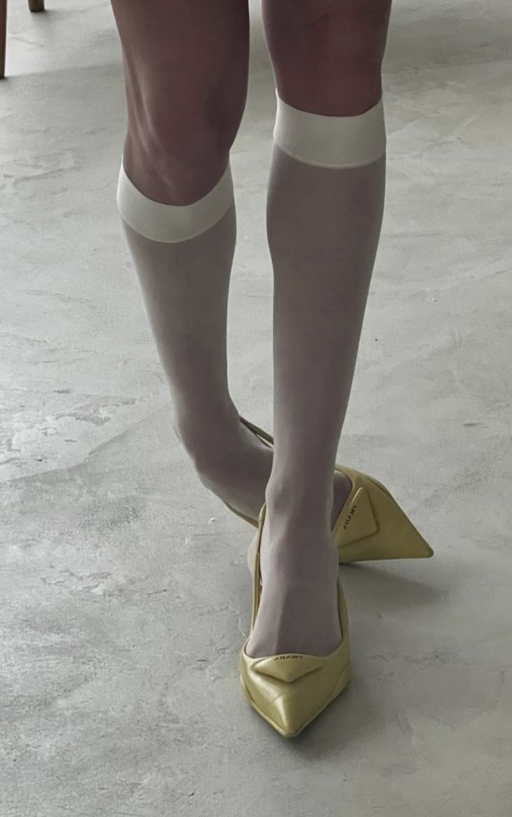 Person wearing white socks and yellow pointed heels on a light-colored floor