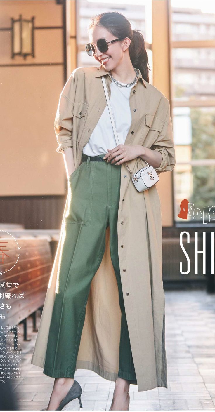 Woman in a long beige coat and green pants, smiling outdoors