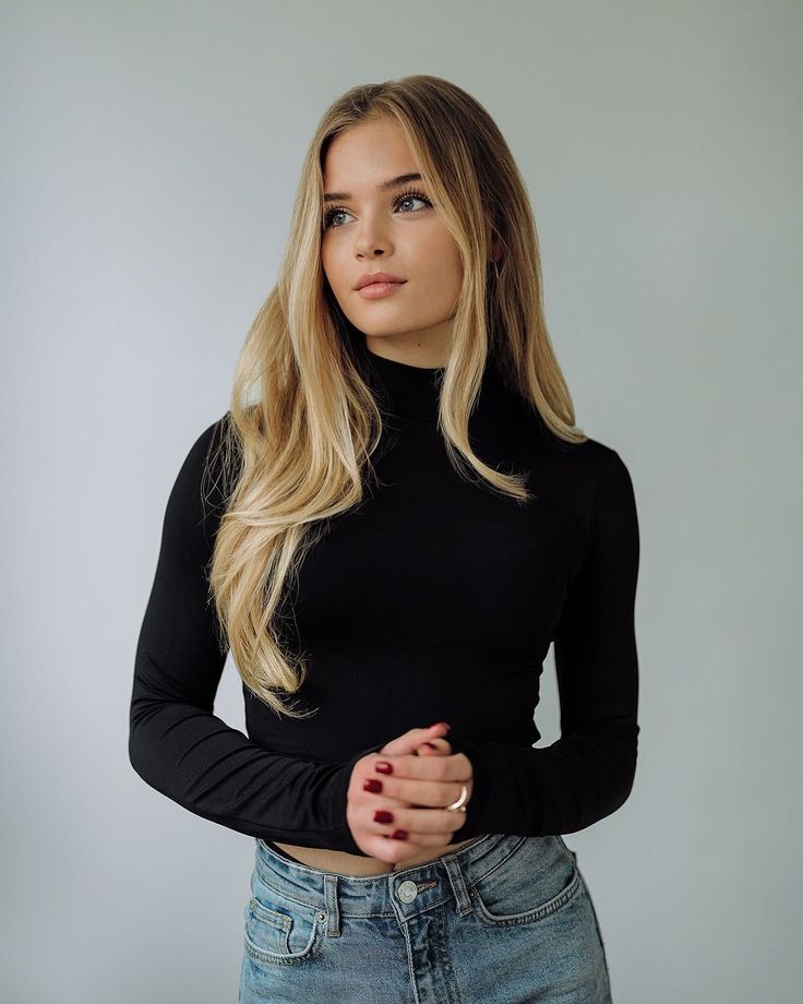 Woman with long blonde hair wearing a black turtleneck and blue jeans indoors