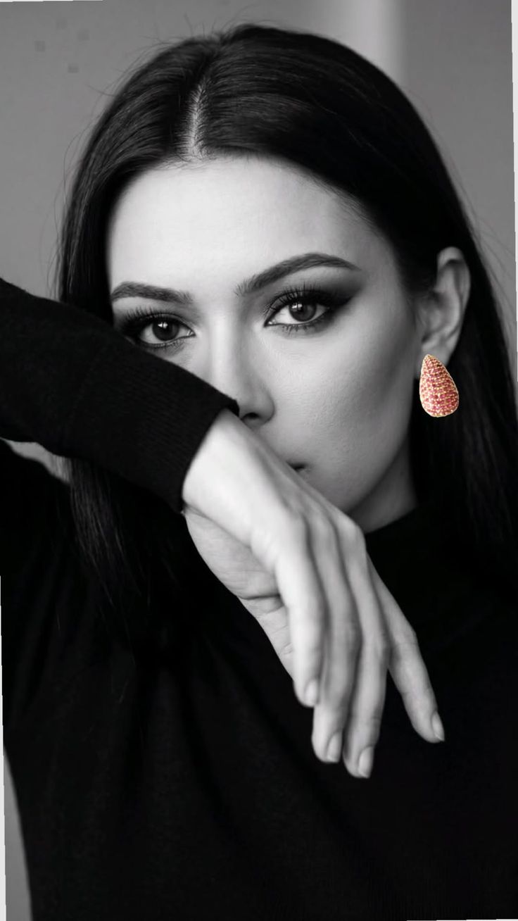 Woman in a black top with an earring, covering her face with her arm