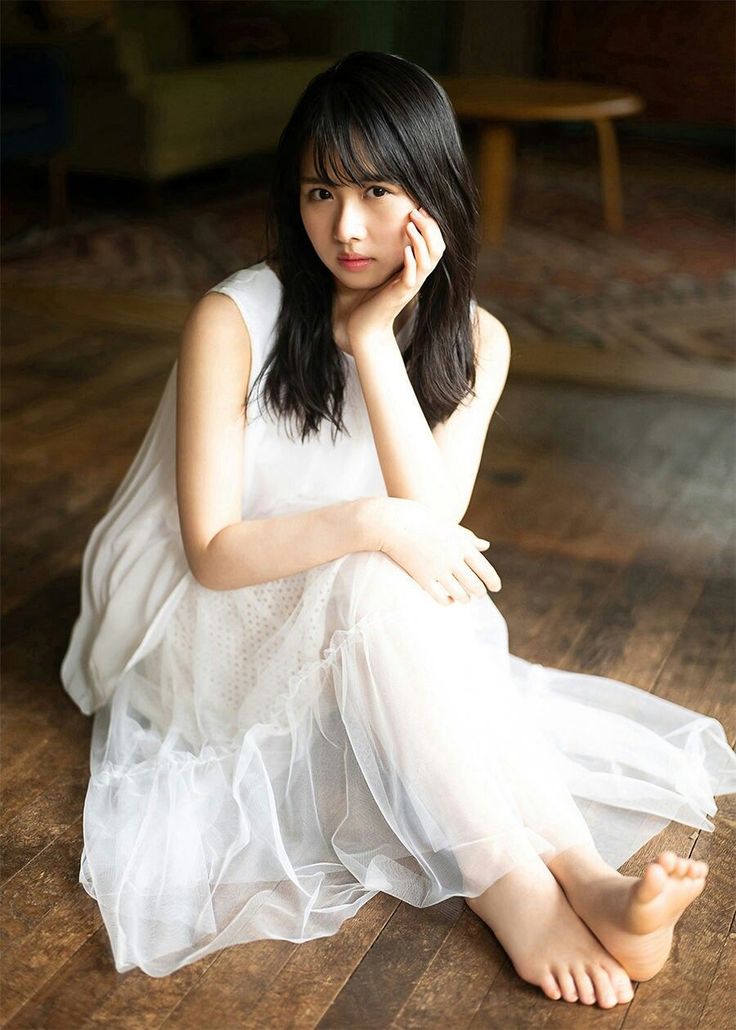 Woman in a white dress sitting barefoot on a wooden floor indoors