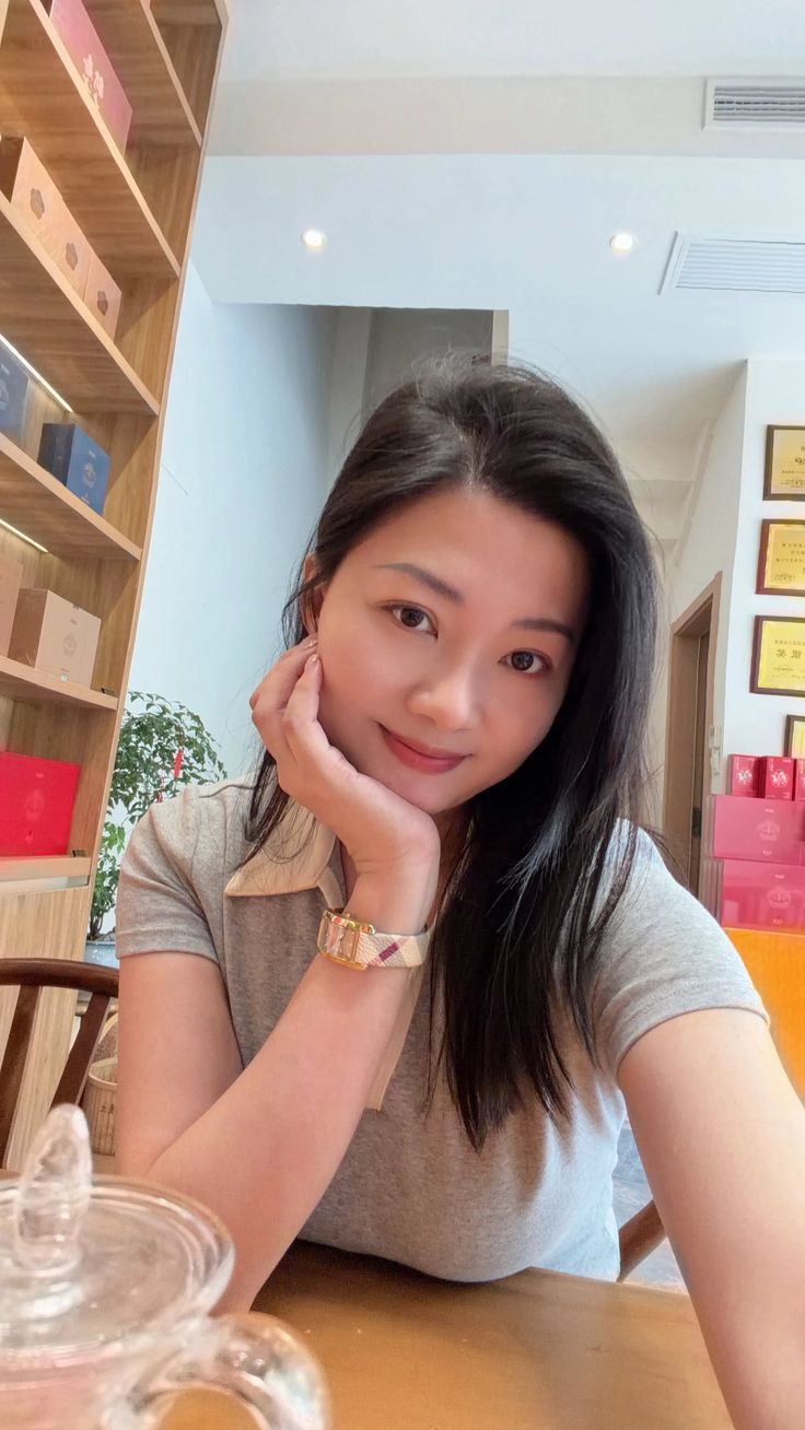 Woman with long dark hair wearing a grey t-shirt and watch, smiling indoors
