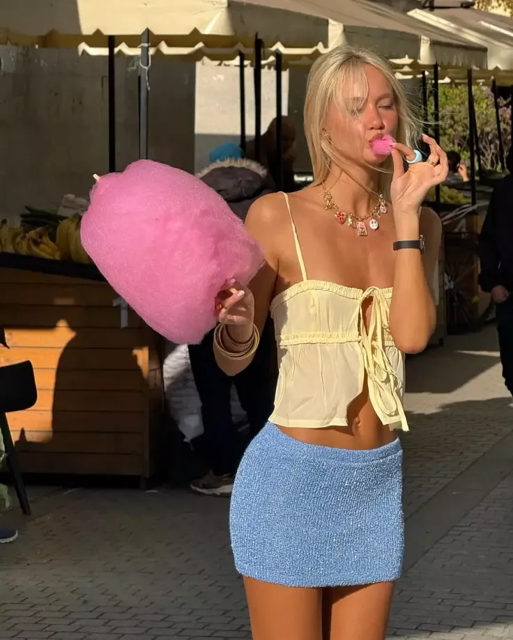 Blonde woman in a crop top and mini skirt eating cotton candy on a street