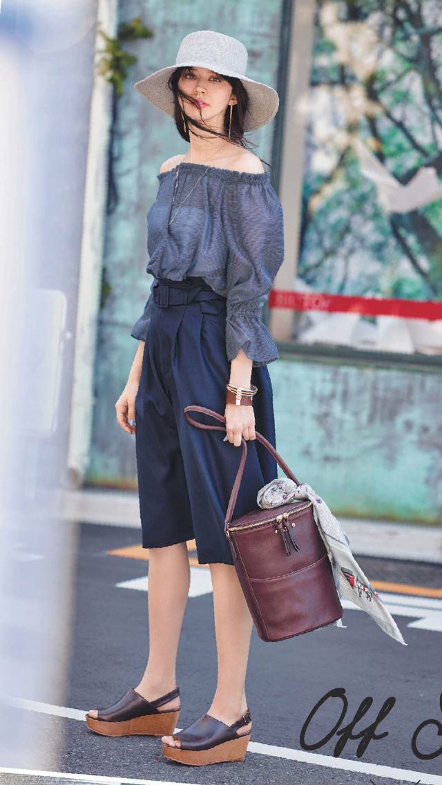 Woman in an off-shoulder top, culottes, and a wide-brim hat holding a handbag