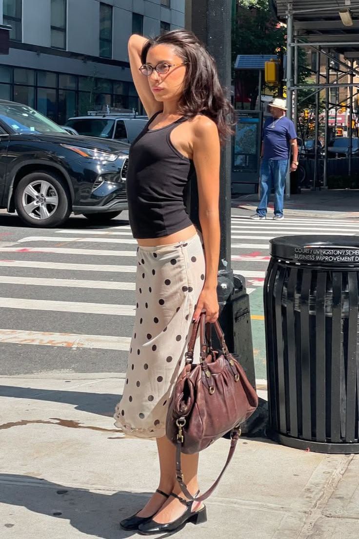 Woman in a black tank top and polka dot skirt on a sunny street