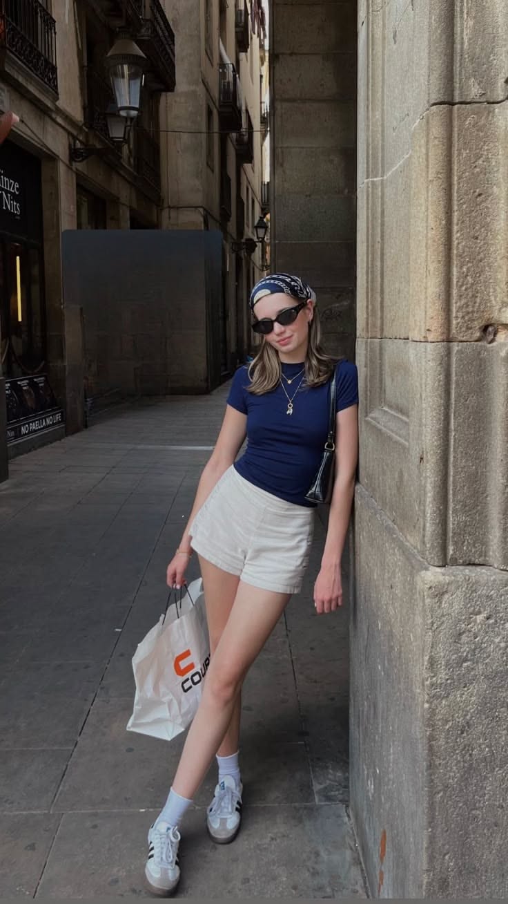 Woman in a bandana and sunglasses leaning against a stone wall on a narrow street