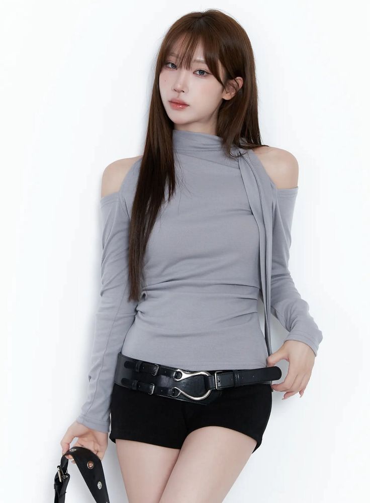 Woman with long hair wearing a gray shoulder cut-out top and black shorts