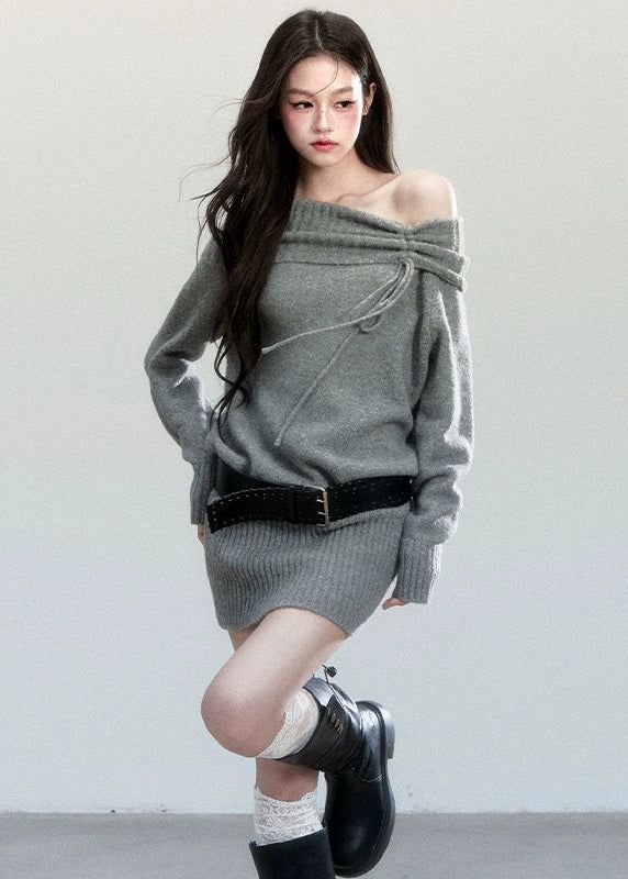 Woman in a gray off-shoulder sweater dress with a black belt and boots