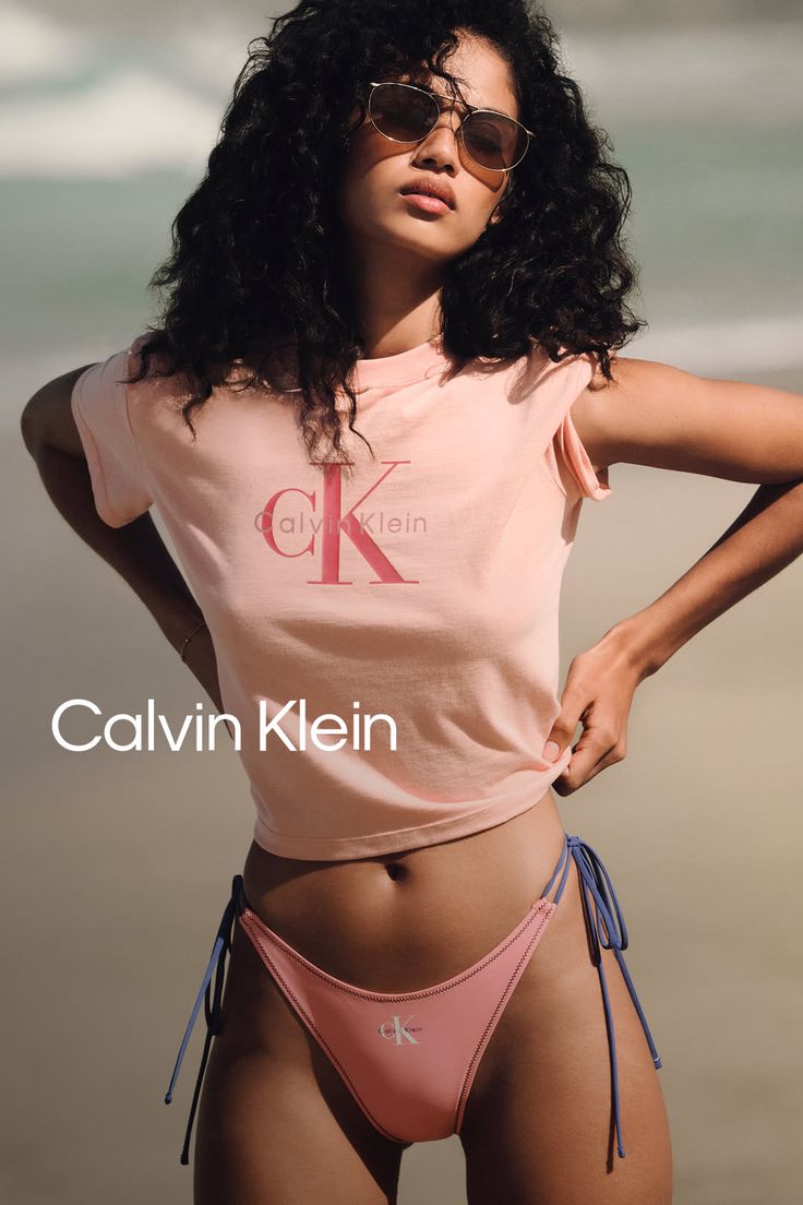 Woman with curly hair and sunglasses wearing a crop top and bikini bottom