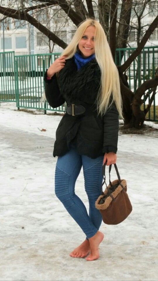 Woman with long blonde hair in a winter coat and jeans standing barefoot in the snow