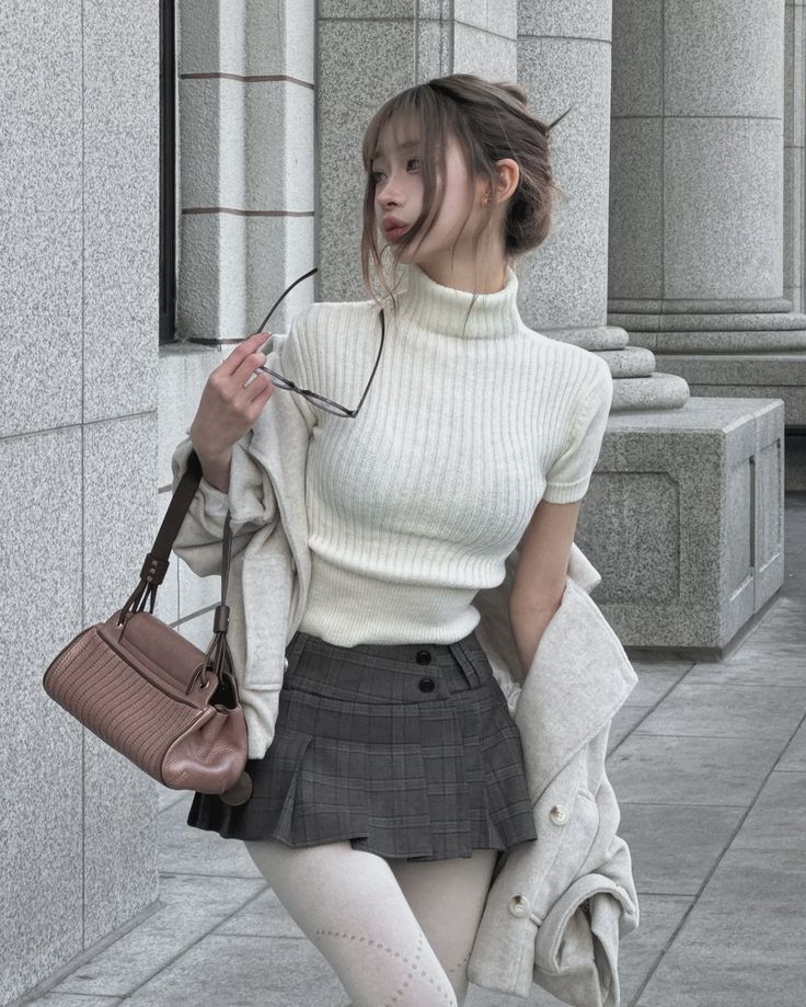 Woman in a white turtleneck and plaid skirt holding glasses outdoors