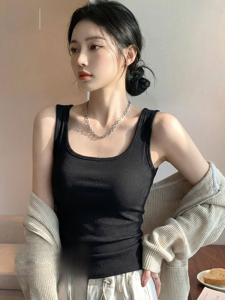 Woman in a black tank top and beige cardigan with hair in a bun