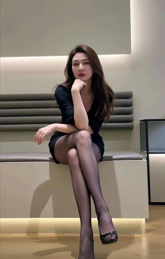 Woman in a black dress and pantyhose sitting indoors with legs crossed