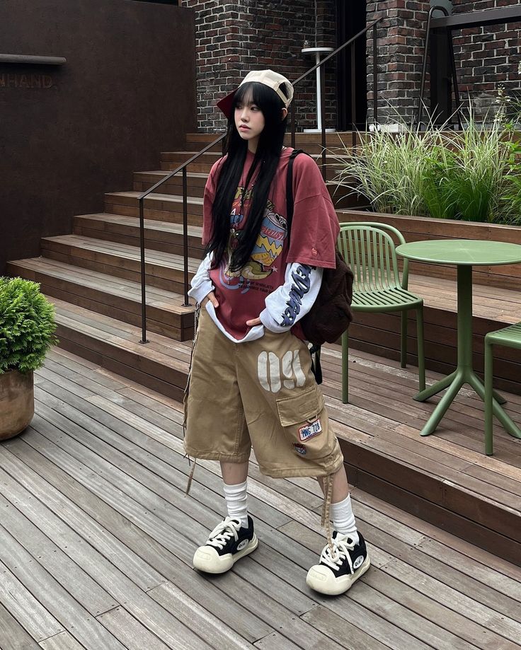 Person with long black hair wearing an oversized t-shirt and cargo shorts outdoors