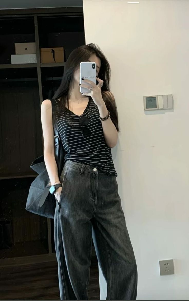 Woman in a striped top and wide leg jeans taking a mirror selfie indoors