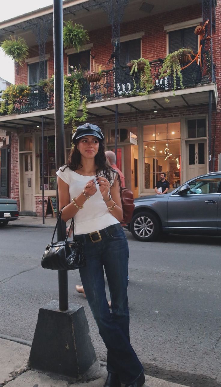 Woman in a white top, jeans, and hat standing on a street
