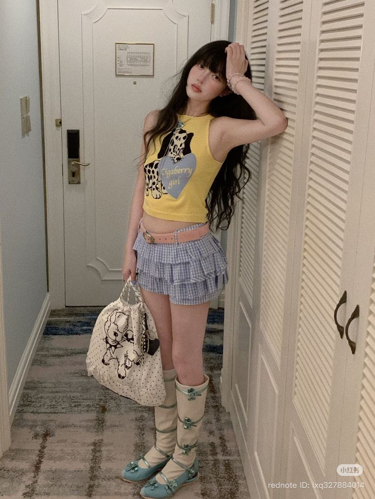 Woman with long hair wearing a yellow crop top and plaid skirt indoors
