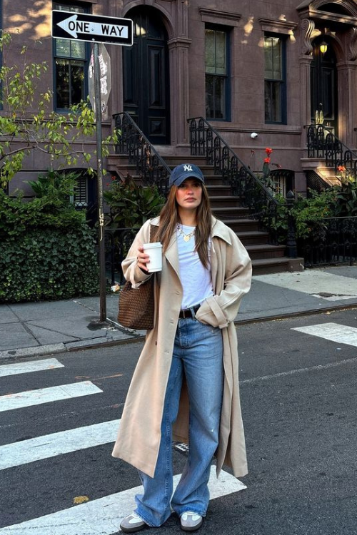 Woman in a trench coat and jeans standing on a city street