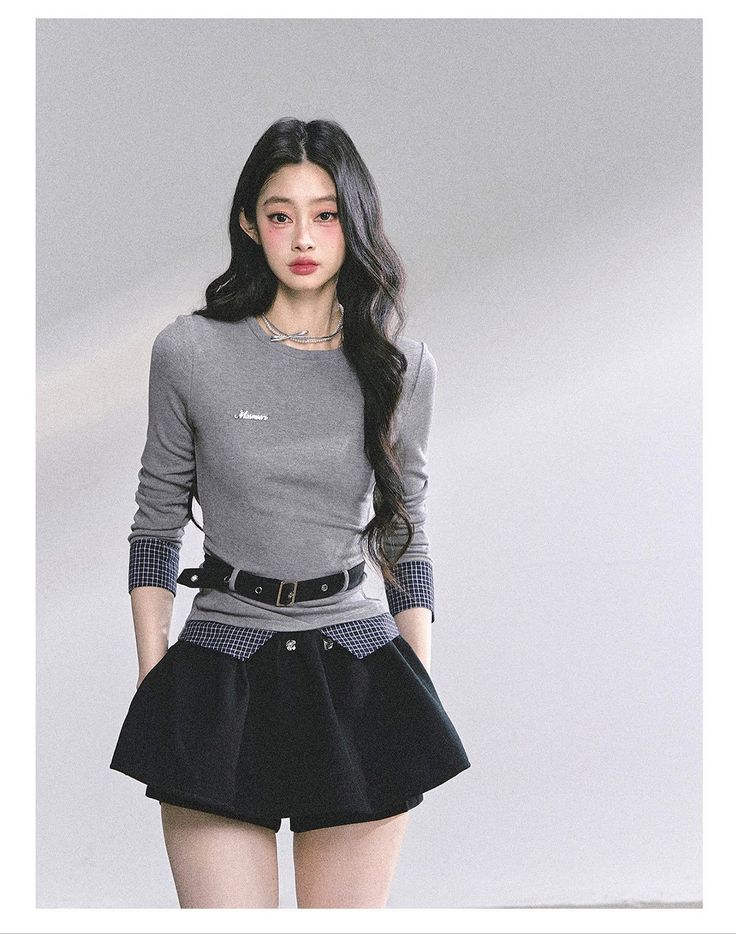 Woman with long black hair wearing a gray top and black skirt indoors