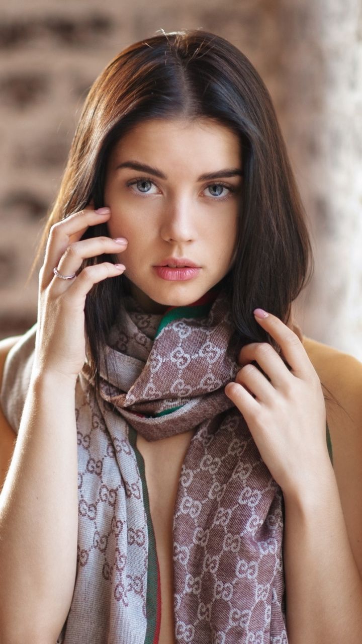 Woman with long dark hair and blue eyes wearing a scarf, with exposed skin