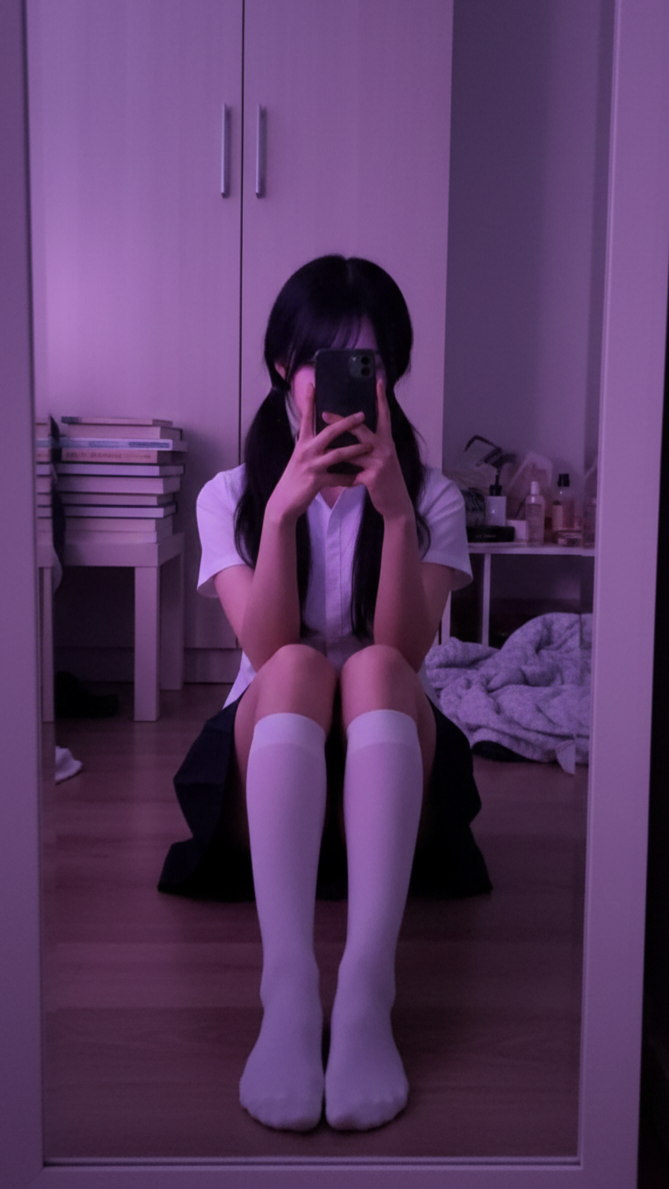 Person in a school uniform taking a mirror selfie while sitting on the floor