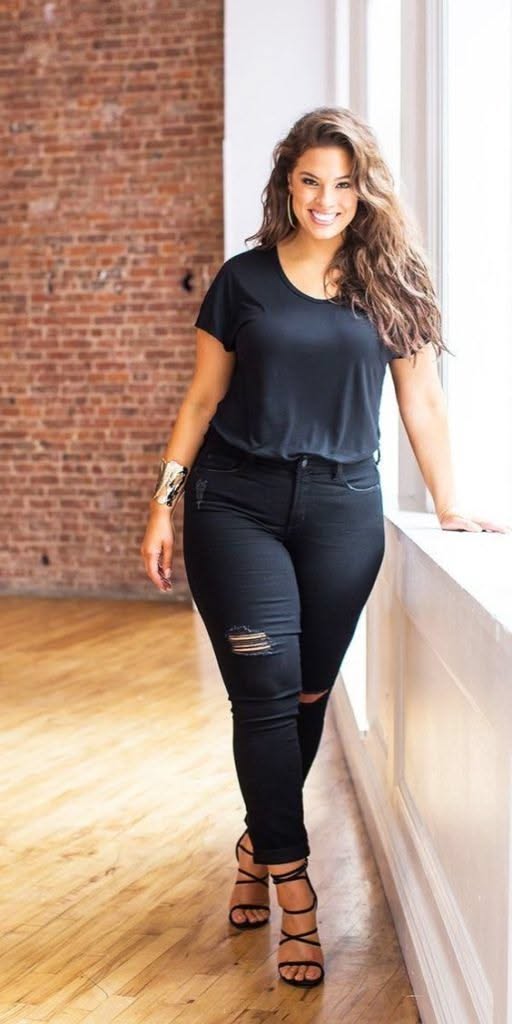 Woman with long hair wearing a black t-shirt and ripped jeans indoors
