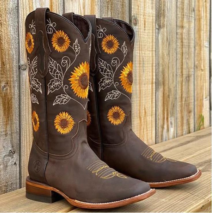 Pair of brown cowboy boots with sunflower embroidery on a wooden surface