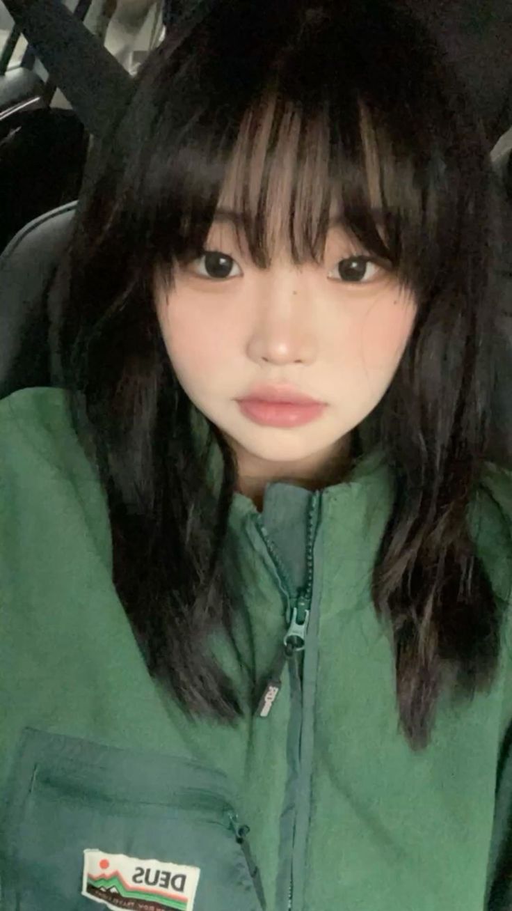 Woman with black hair and bangs wearing a green jacket, close up