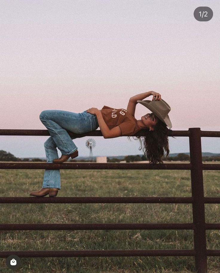 Woman in a cowboy hat and jeans lying on a fence in the countryside at sunset