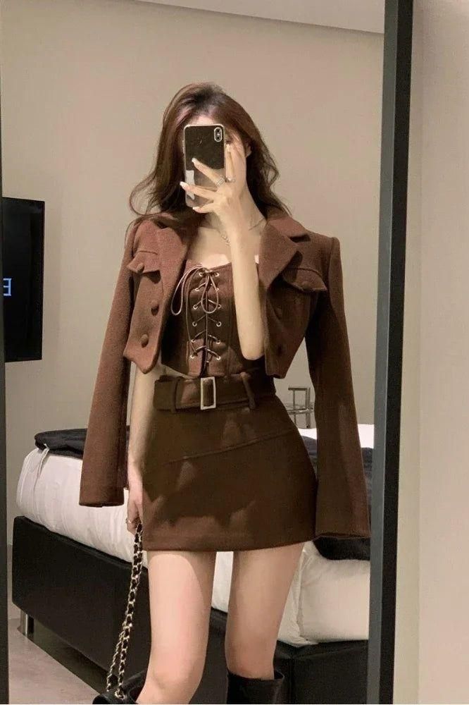 Woman in a brown cropped jacket, corset top, and mini skirt taking a mirror selfie