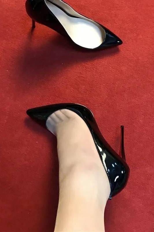 A pair of black high heels on a red carpet, one worn on a foot