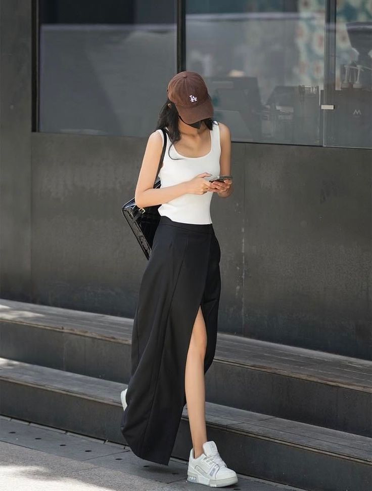 Woman in a white tank top and black skirt with a brown baseball cap walking outdoors